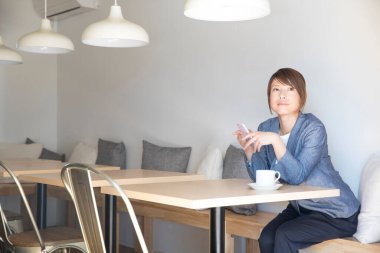 Genç bir kadın kahve içiyor ve akıllı telefon kullanıyor. 