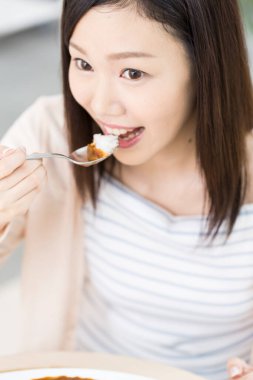 Restoranda kaşıkla pirinç yiyen Asyalı bir kadın..