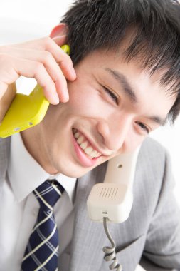 İki telefonla konuşan genç Japon iş adamının yakın plan portresi.