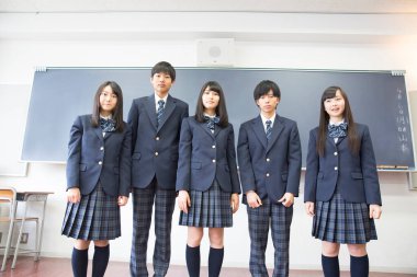 Sınıfta duran üniformalı öğrencilerin fotoğrafı.