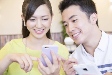 Ofiste akıllı telefon kullanan Asyalı genç ve neşeli bir çift.