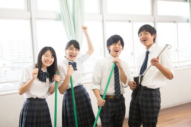 Sınıfı süpürgelerle temizleyen mutlu öğrenciler.