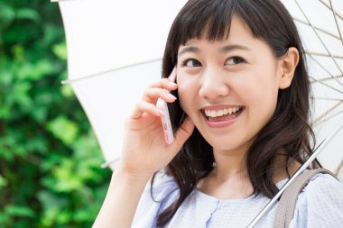 Şemsiyeli genç Asyalı kadın dışarıda akıllı telefondan konuşuyor. 