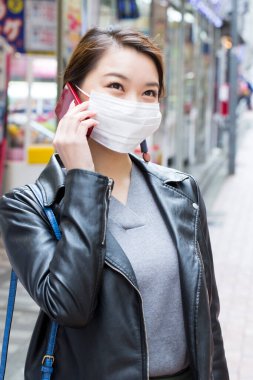 Yüz maskesi takan Asyalı kız akıllı telefondan konuşuyor. 