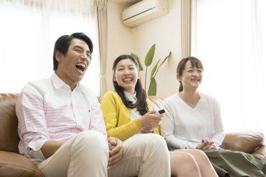  Uzaktan kumandalı Asyalı anne, baba ve kızı kanepede oturup televizyon izliyor. 