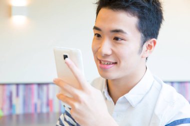 Young man using smartphone while studying in modern cafe