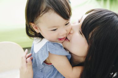 Genç Asyalı anne ve küçük kız öpüşüyor ve sarılıyorlar.
