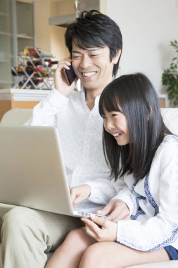 Asyalı genç baba ve kızı evde dizüstü bilgisayar kullanıyorlar.