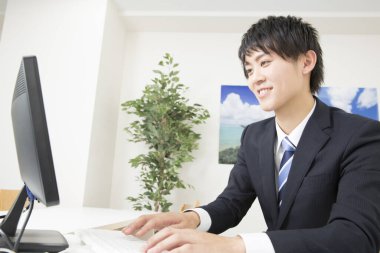 Genç Asyalı işadamı ofiste çalışırken bilgisayar kullanıyor.