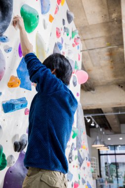 Kayalık spor salonunda yapay tırmanma duvarına tırmanan bir adam.