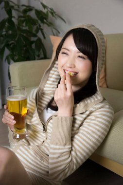 Genç Asyalı kadın bira ve atıştırmalıklarla dinleniyor.