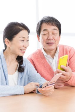 Üst düzey Asyalı çift evde telefondan haber okuyor.