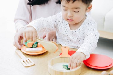 Asyalı anne ve oğlu evde tahta oyuncaklarla oynuyorlar. 