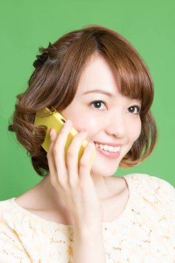 Güzel Japon kadının portresi yeşil arka planda akıllı telefondan konuşuyor. 