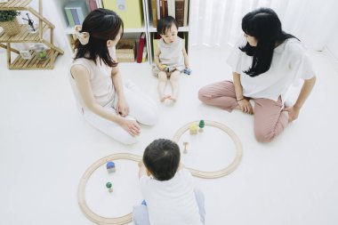 Neşeli Asyalı anneler ve çocuklar oturma odasında oynuyor.