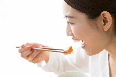 Asyalı kadın evde çubuklarla yemek yiyor.