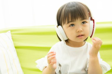 Kanepede kulaklık takan küçük Asyalı çocuk.