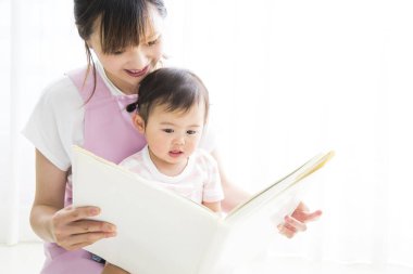 Asyalı anaokulu öğretmeni ve odada kitap okuyan sevimli küçük kız.