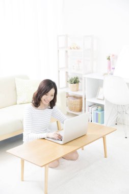 Evde dizüstü bilgisayar kullanan gülümseyen Asyalı kadın.