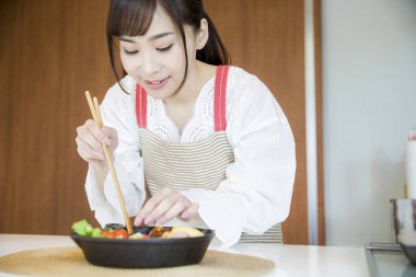 Asyalı kadın evde çubuklarla yemek yiyor. 