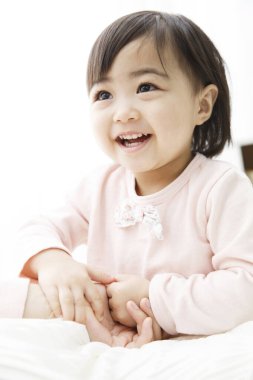 Asyalı bebek gülümsüyor ve annesinin elini tutuyor. 