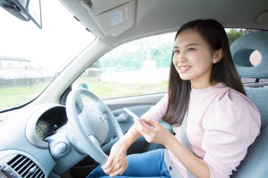 Asyalı genç bir kadın akıllı telefonuyla arabada oturuyor. 