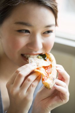 Kadın bir dilim pizza yiyor.