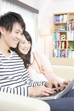 Mutlu Asyalı çift evde dizüstü bilgisayar kullanıyor.