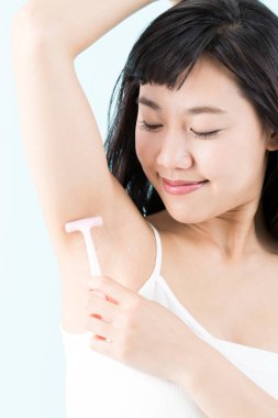 Tüylerini aldırmak için koltuk altını tıraş eden genç bir kadın.