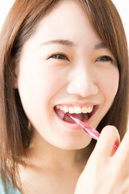 Genç bir Asyalı kadın dişlerini fırçalıyor.