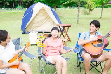 Mutlu Asyalı arkadaşlar kamp parkında müzik aletleri çalıyorlar.