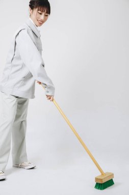 Asyalı bir kadın gri arka planda yerleri paspaslıyor. 