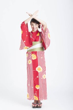 Kimonolu genç bir Asyalı kadın ellerini çapraz yapıp beyaz arka planda izole bir şekilde hareket ediyor.