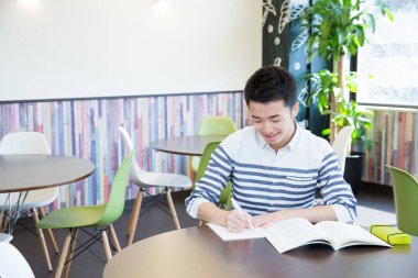 Asyalı öğrenci üniversitede masada okuyor. 