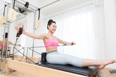 sporty Japanese woman in sportswear training with reformer indoors clipart