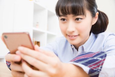 Asyalı kadın oturma odasında akıllı telefon kullanıyor.