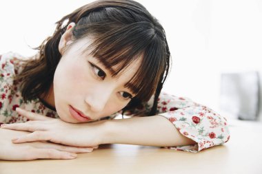 Kollarını kavuşturup masada oturan üzgün Asyalı kadının portresi.