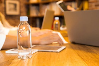 Ofiste çalışan genç adamın dizüstü bilgisayarı ve bir şişe su ile yakın plan fotoğrafını çek.