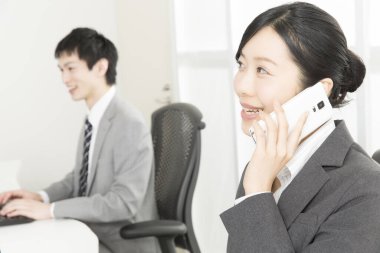 Bilgisayarla çalışan genç adam ve telefonda konuşan iş arkadaşı kadın. 