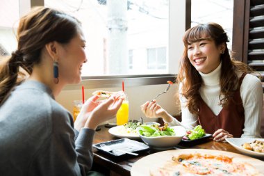 Kahvede yemek yiyen gülümseyen Japon kadınlar.