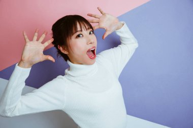 Beyaz kazaklı, elleri havada Asyalı kadın portresi.