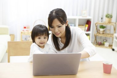 Genç anne ve küçük kızı evde dizüstü bilgisayar kullanıyorlar.