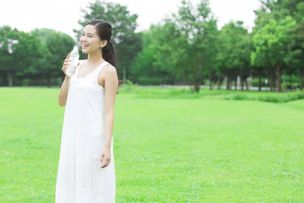 美丽的日本女人白天在绿色的夏季公园喝水 — 图库照片
