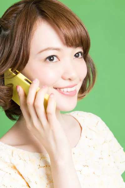 漂亮的日本女人在绿色背景的智能手机上说话的肖像 — 图库照片