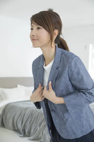 asian woman putting on jacket and looking at mirror