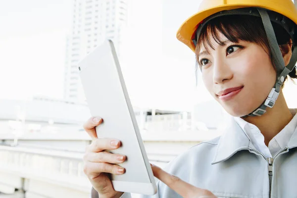 young asian woman engineer in helmet holding tablet pc