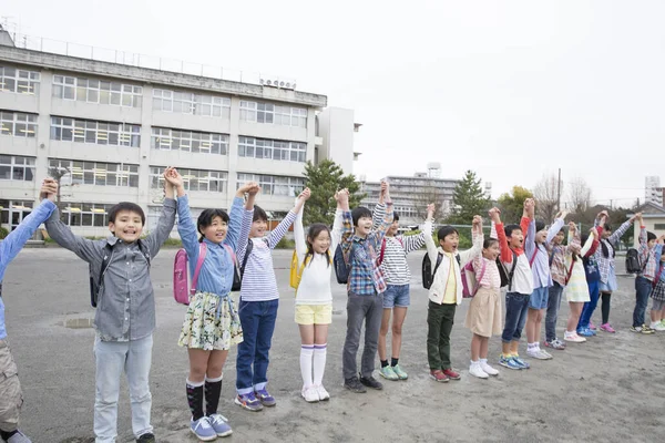 Okul bahçesinde el ele tutuşan bir grup Japon çocuk. 