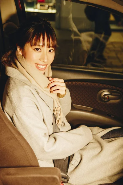 穿着秋装的年轻日本女人坐在现代汽车上 朦胧地照亮着城市的背景 — 图库照片