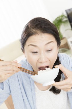 Asyalı kadın çubuklarla pirinç yiyor. 