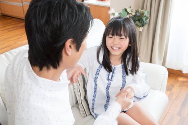 Mutlu genç Japon baba ve kızı kanepede el ele tutuşuyorlar. 